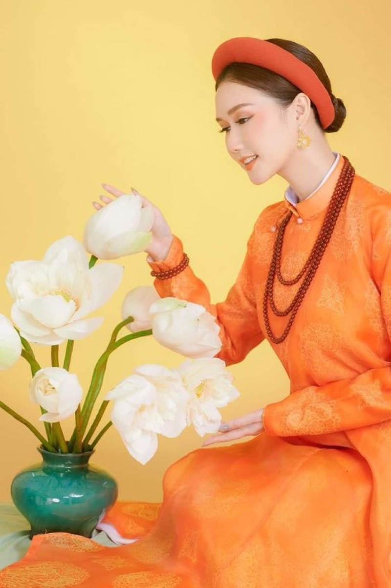 Thiếu nữ áo dài cam nổi bật bên bình hoa sen trắng