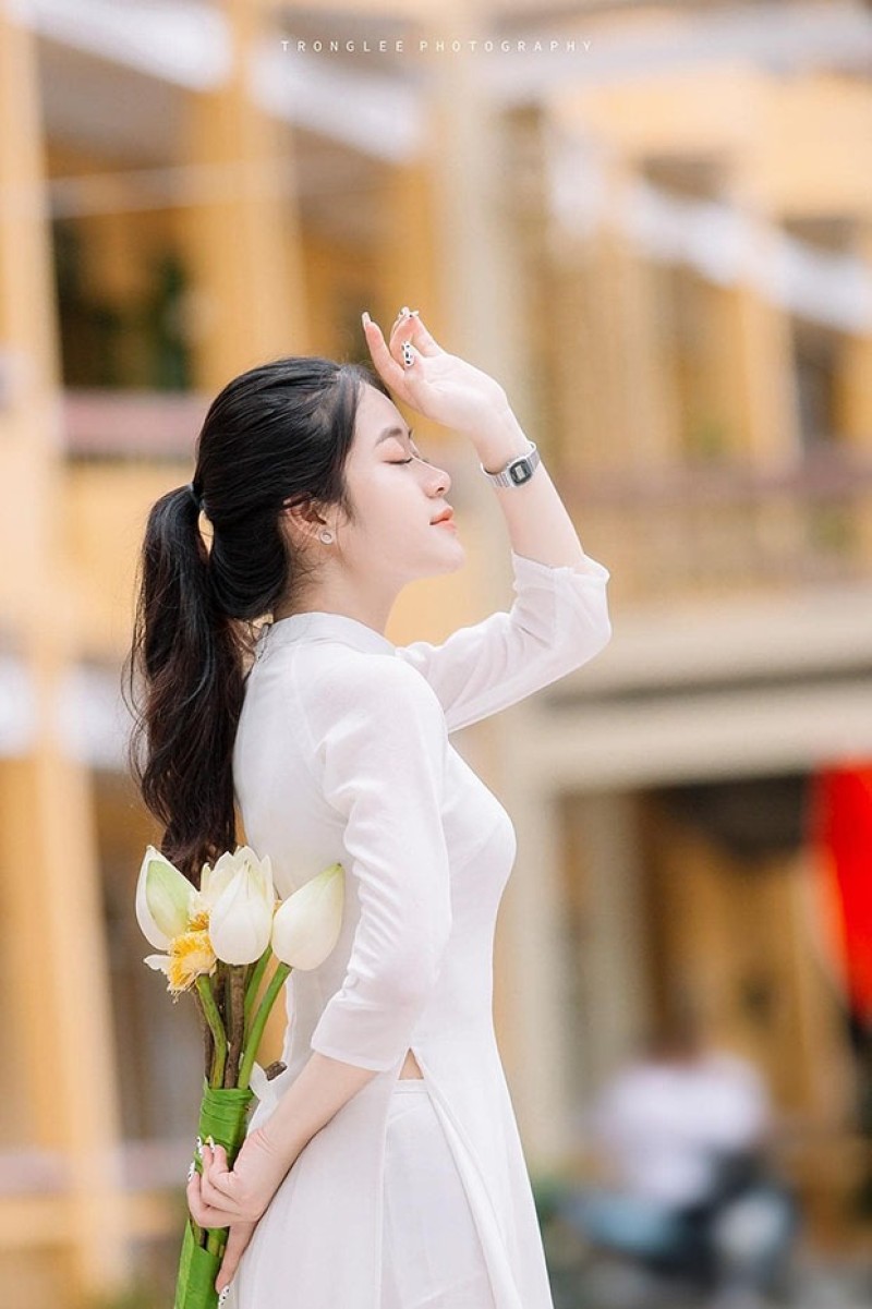 Đứng thẳng tay trái đặt sau lưng cầm hoa, tay phải dơ lên trán, mỉm cười